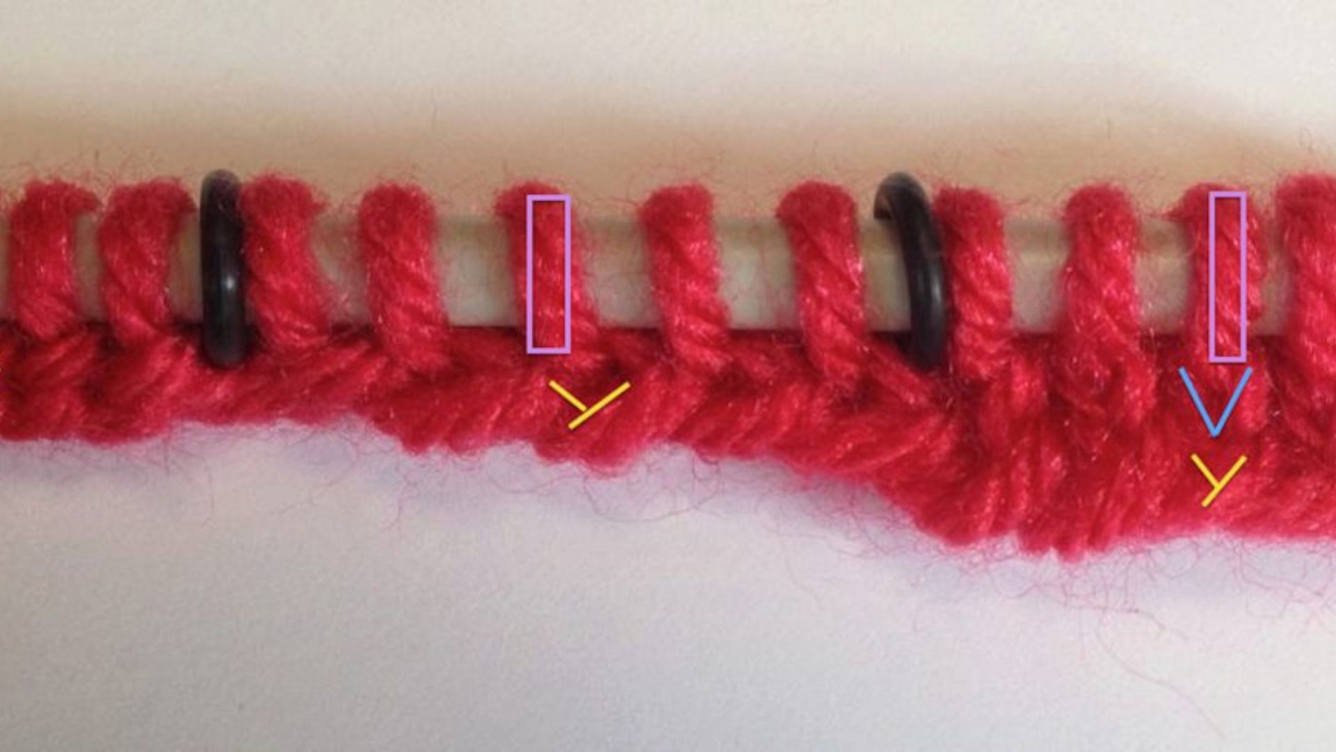 A red yarn is being knitted with a black needle, showcasing the process of creating a knitted item.