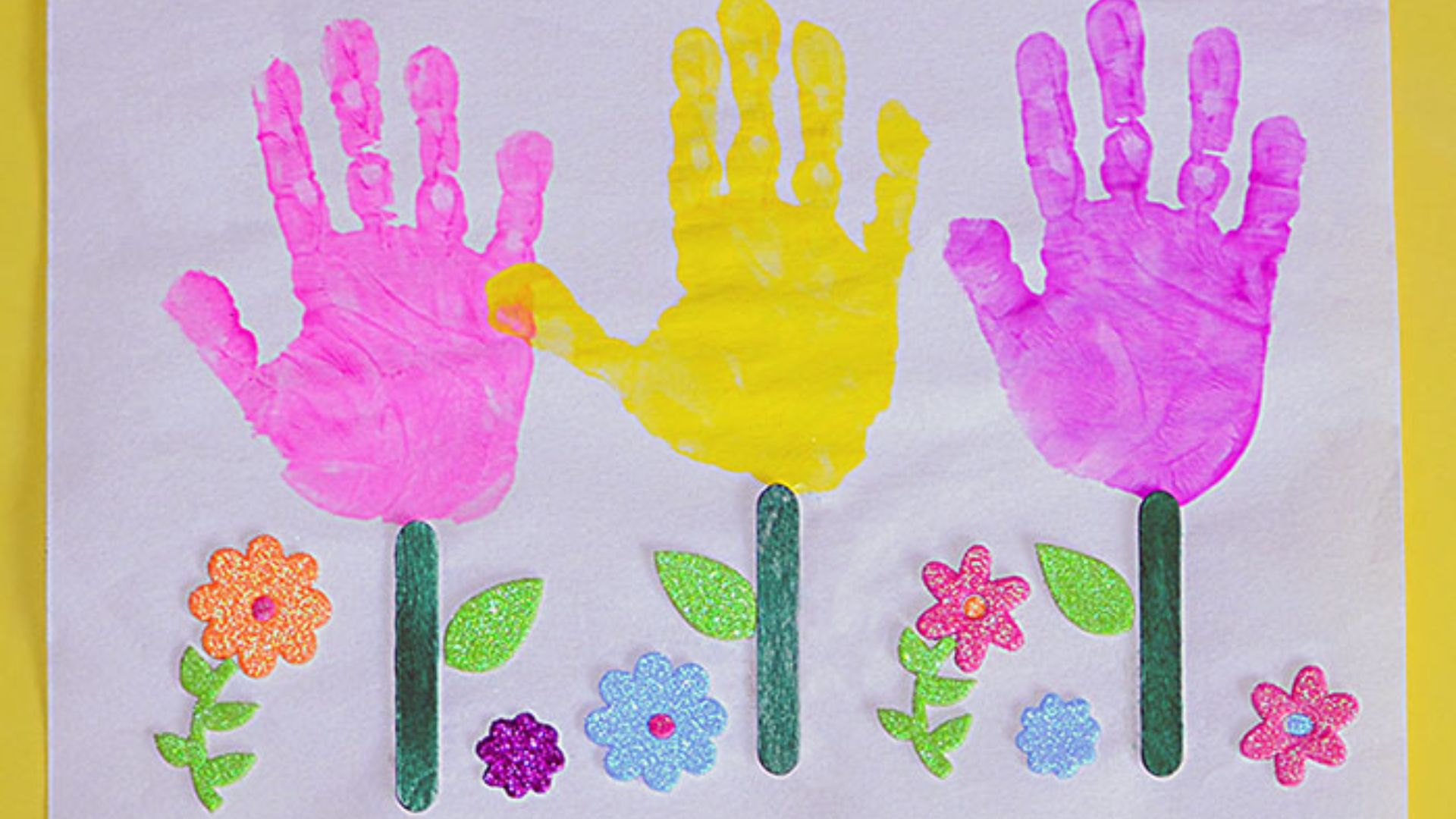 A creative handprint flower craft for children, featuring bright handprint petals and a simple green stem design.