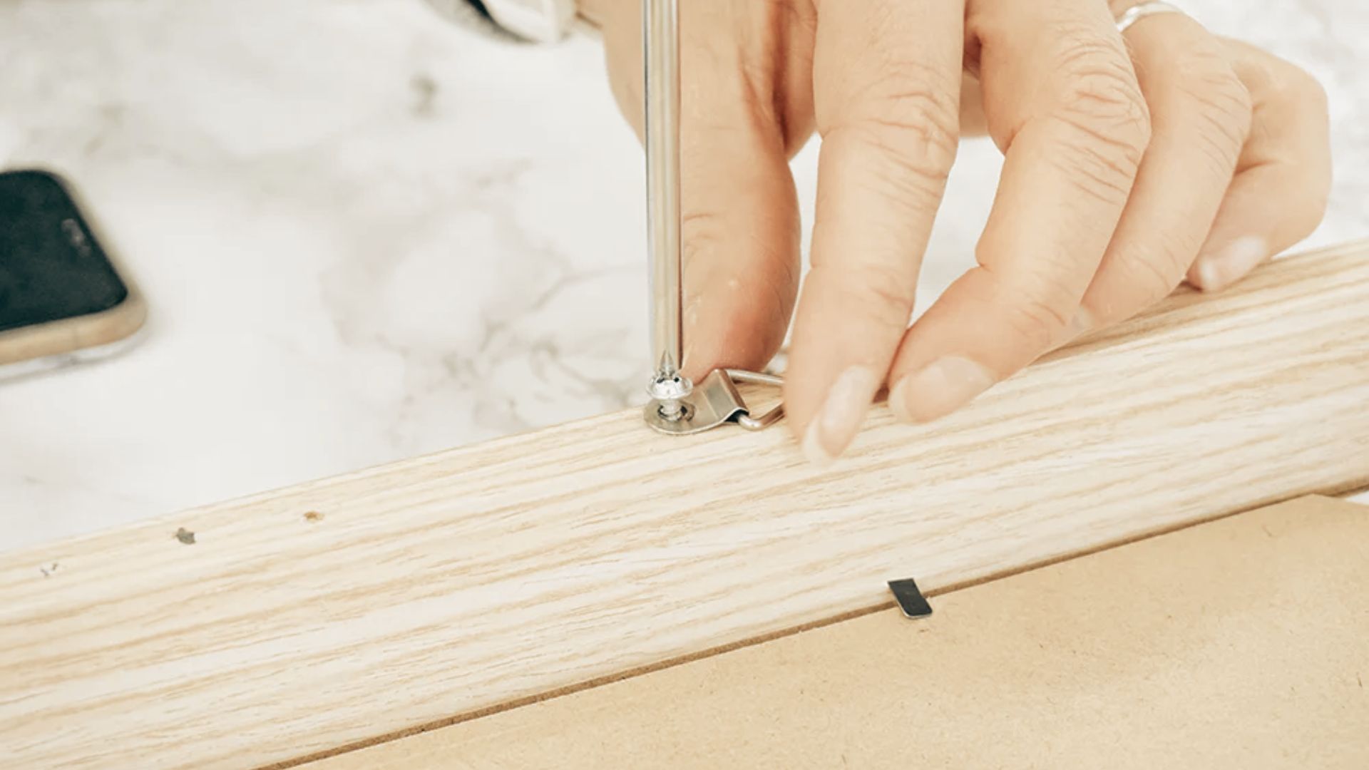 A person uses a screwdriver to fasten one piece of wood to another in a woodworking project.