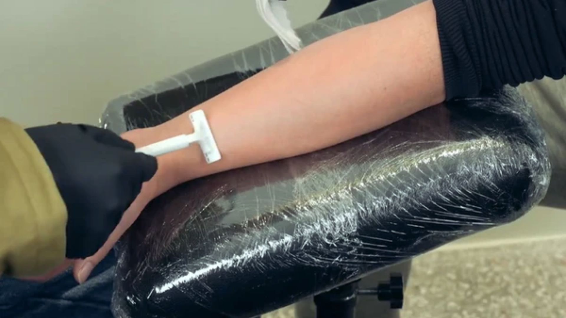 A person sitting in a chair while a healthcare professional draws blood with a needle from their arm.