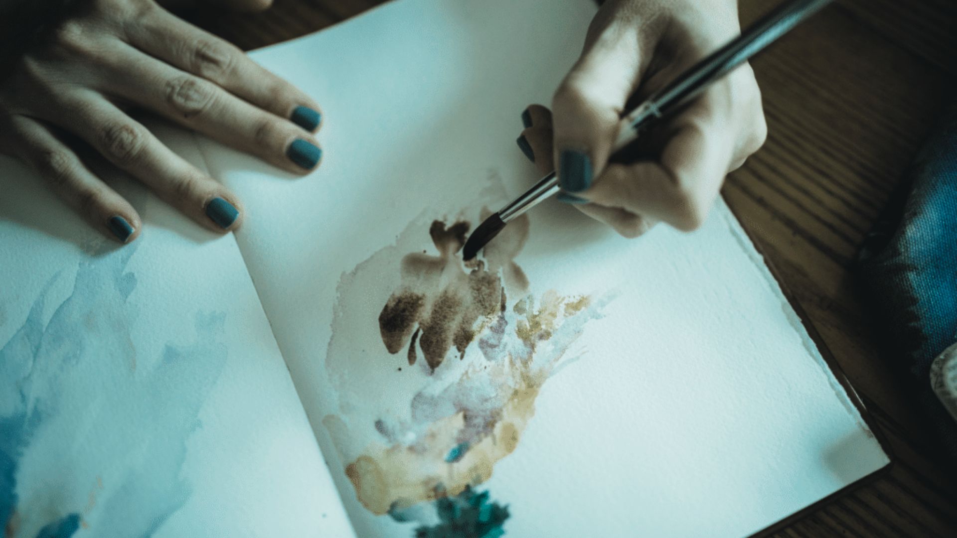 A person holds a brush, painting on a piece of paper with vibrant colors and focused expression.