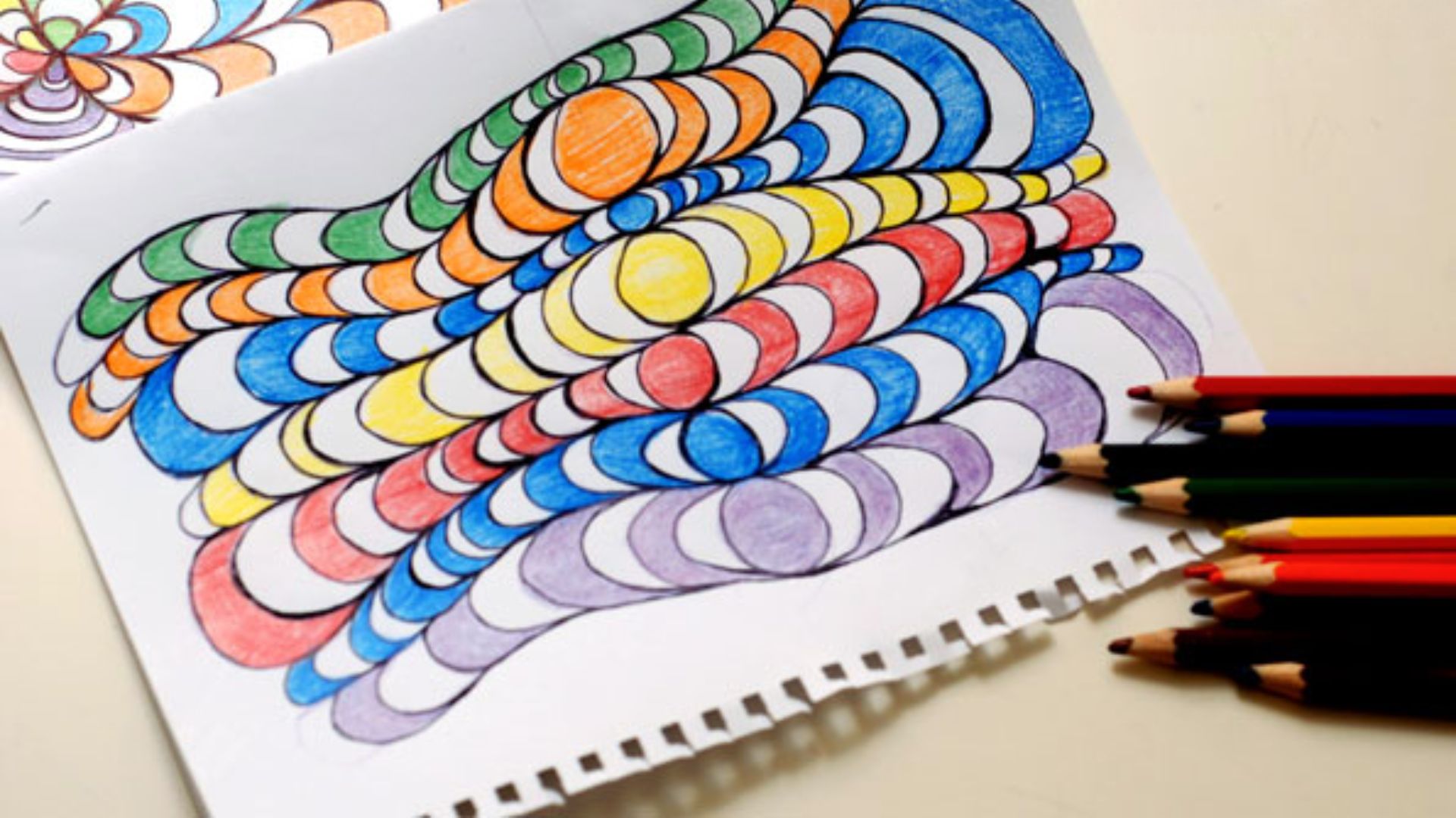 A coloring book open to a page with colorful circles and a pencil resting beside it.