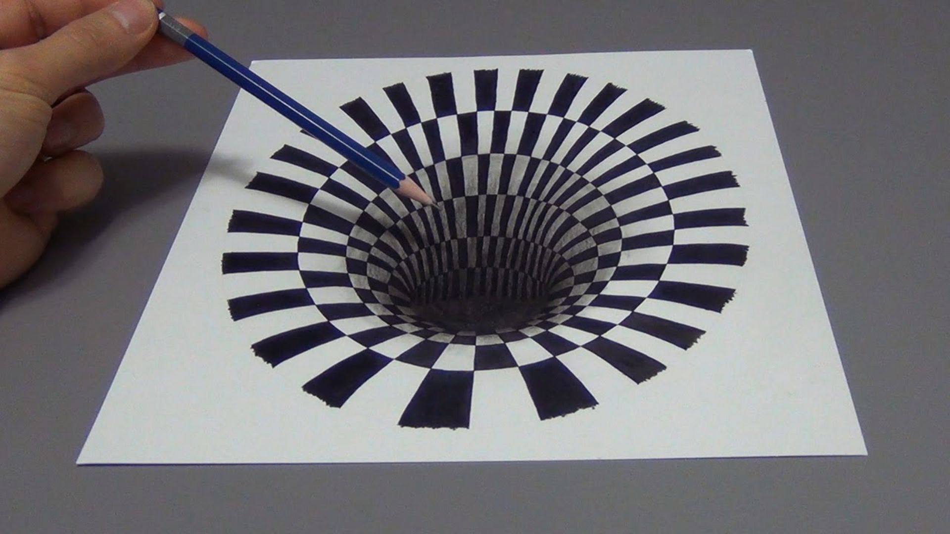 A person sketches a detailed black and white pattern on a sheet of paper, focusing intently on their work.