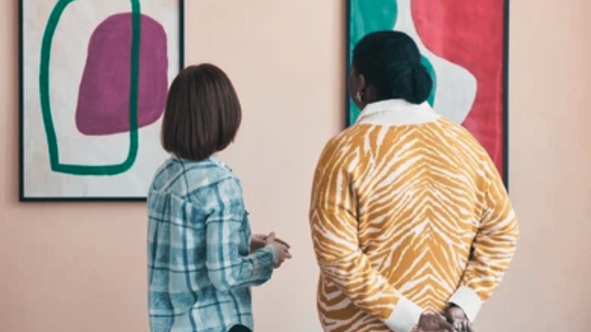 wo women observing artwork in a contemporary art gallery, engaged in discussion about the pieces displayed.