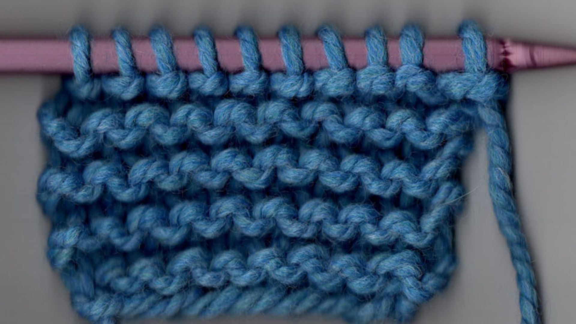 A knitting needle holds a strand of blue yarn, showcasing the beginning of a knitting project.