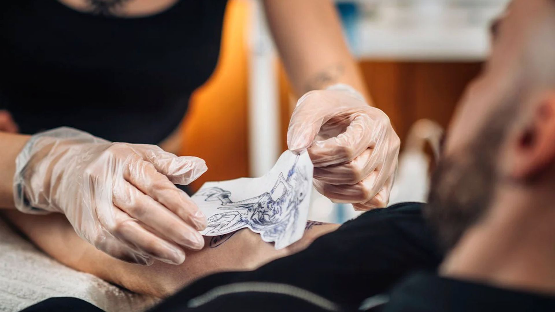 A man receiving a tattoo on his arm, focused on the artist's work and the design being inked.
