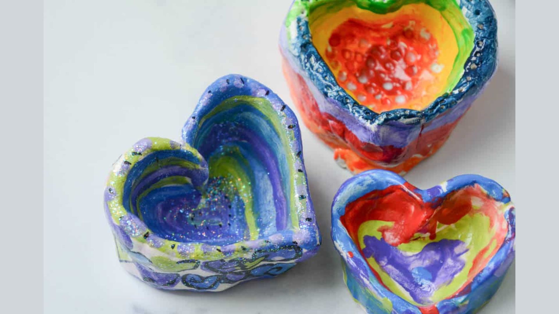 Three vibrant heart-shaped bowls in red, blue, and yellow are arranged on a wooden table.