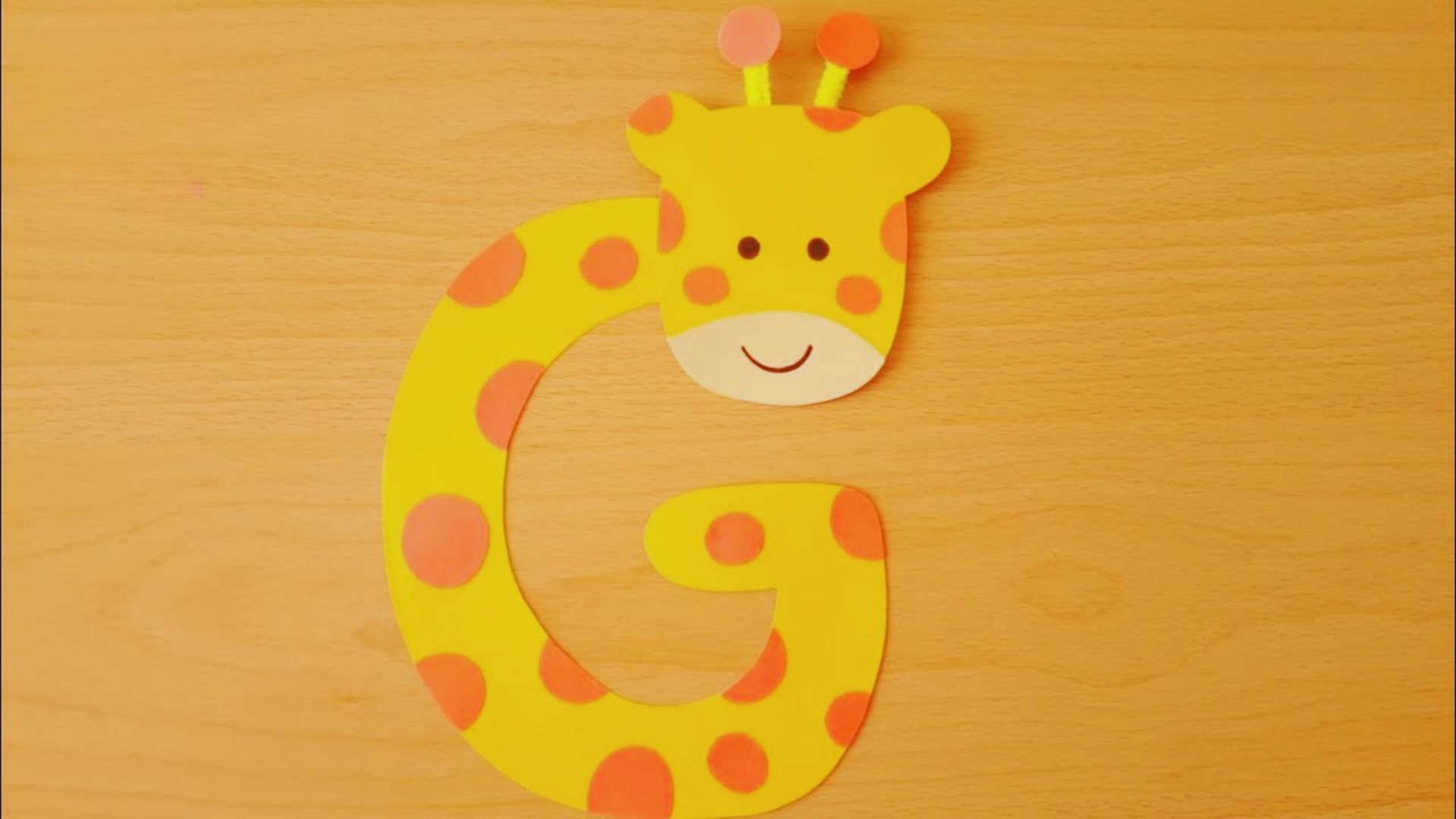 A paper cutout of a giraffe next to the letter 'g' on a plain background, illustrating the letter's association with the animal.