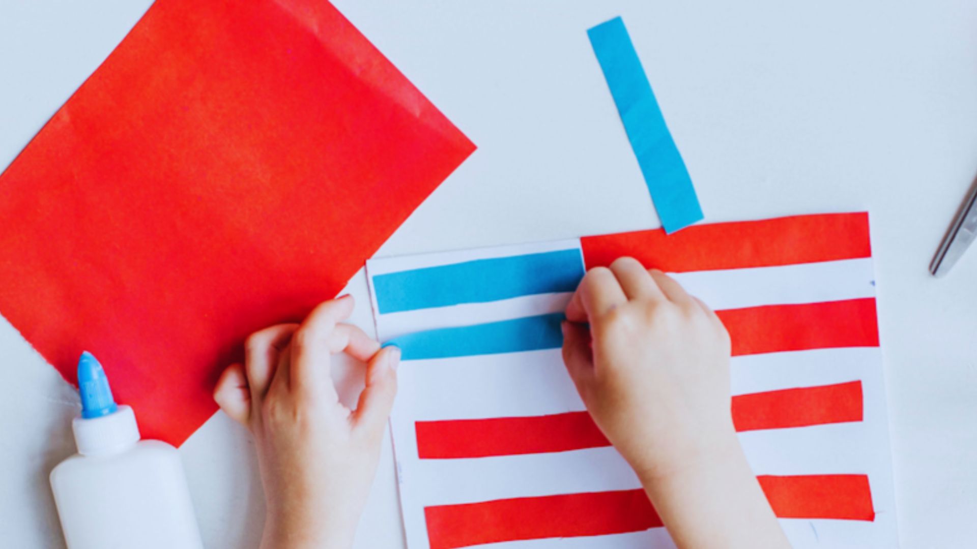 A child cuts paper with red, white, and blue stripes for a Cut-and-Paste American Flag craft project