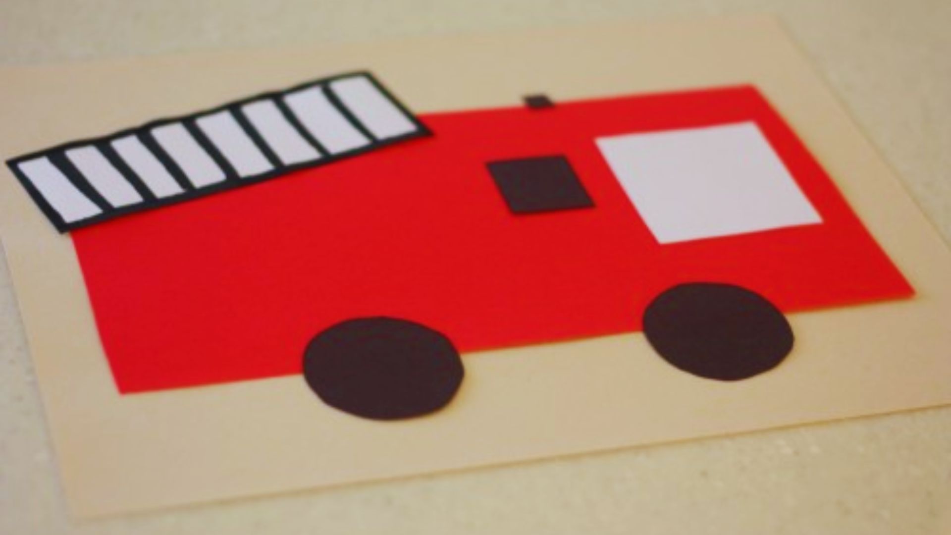 Colorful fire truck craft made from construction paper, featuring wheels, ladder, and a bright red design for kids' activities.