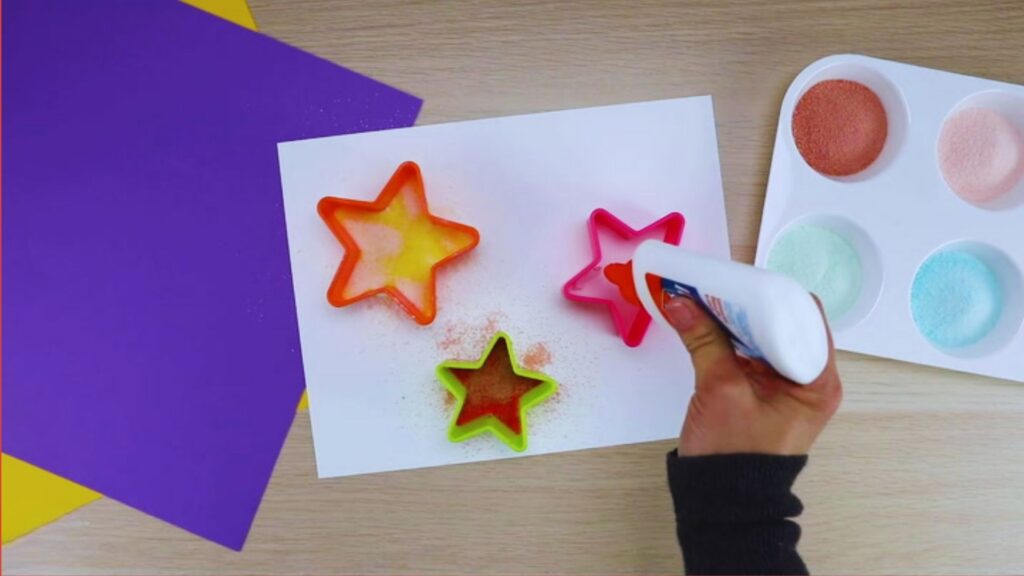 A person using a glue gun to decorate star-shaped cookies as part of a toddler art and craft activity.
