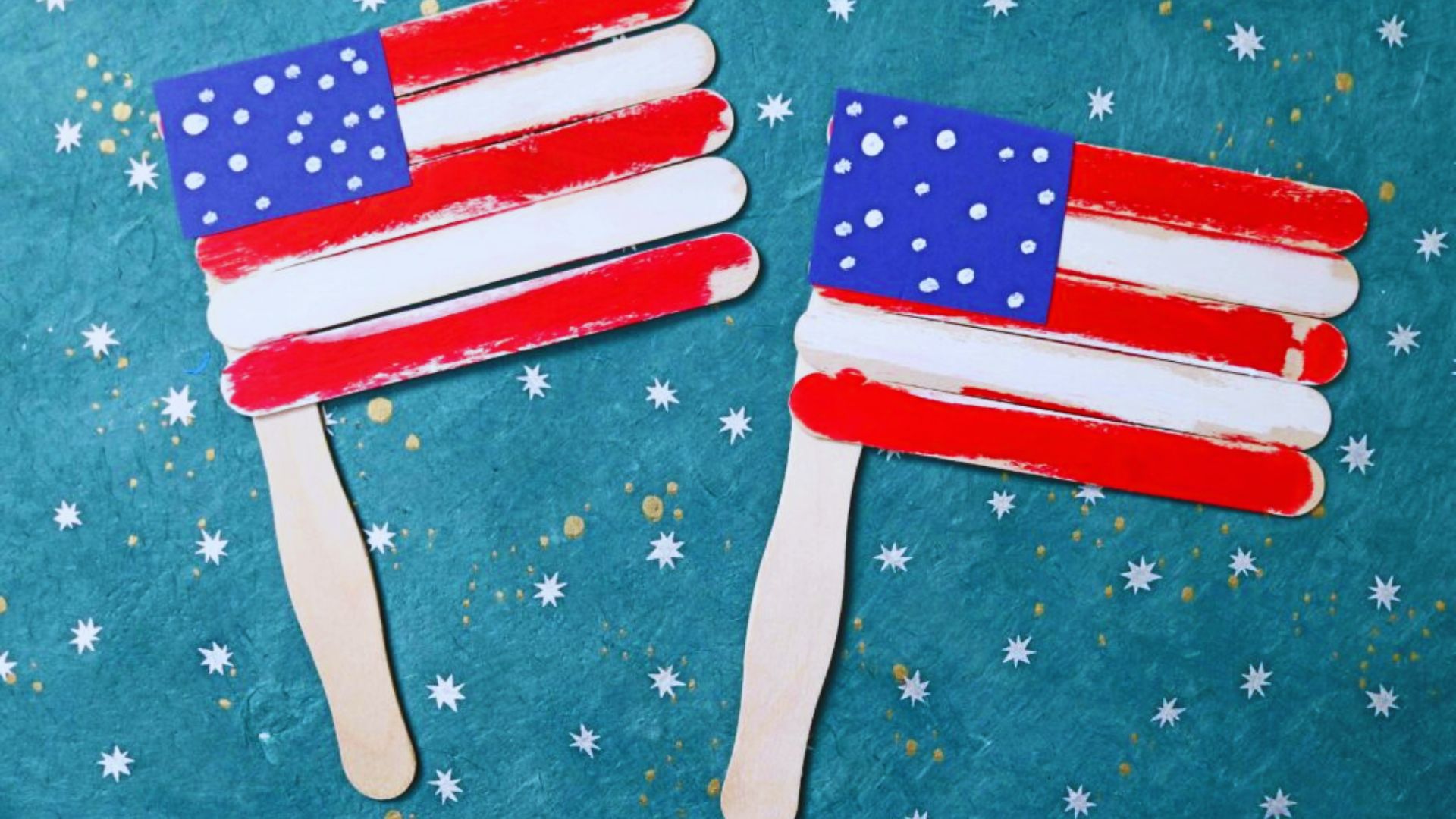 Two popsicle sticks decorated as American flags on a green background, showcasing an ice cream stick flag banner craft.