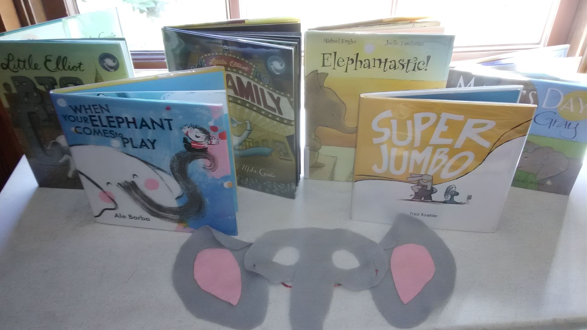 A colorful elephant craft made from paper, featuring large ears and a trunk, displayed on a table with art supplies.