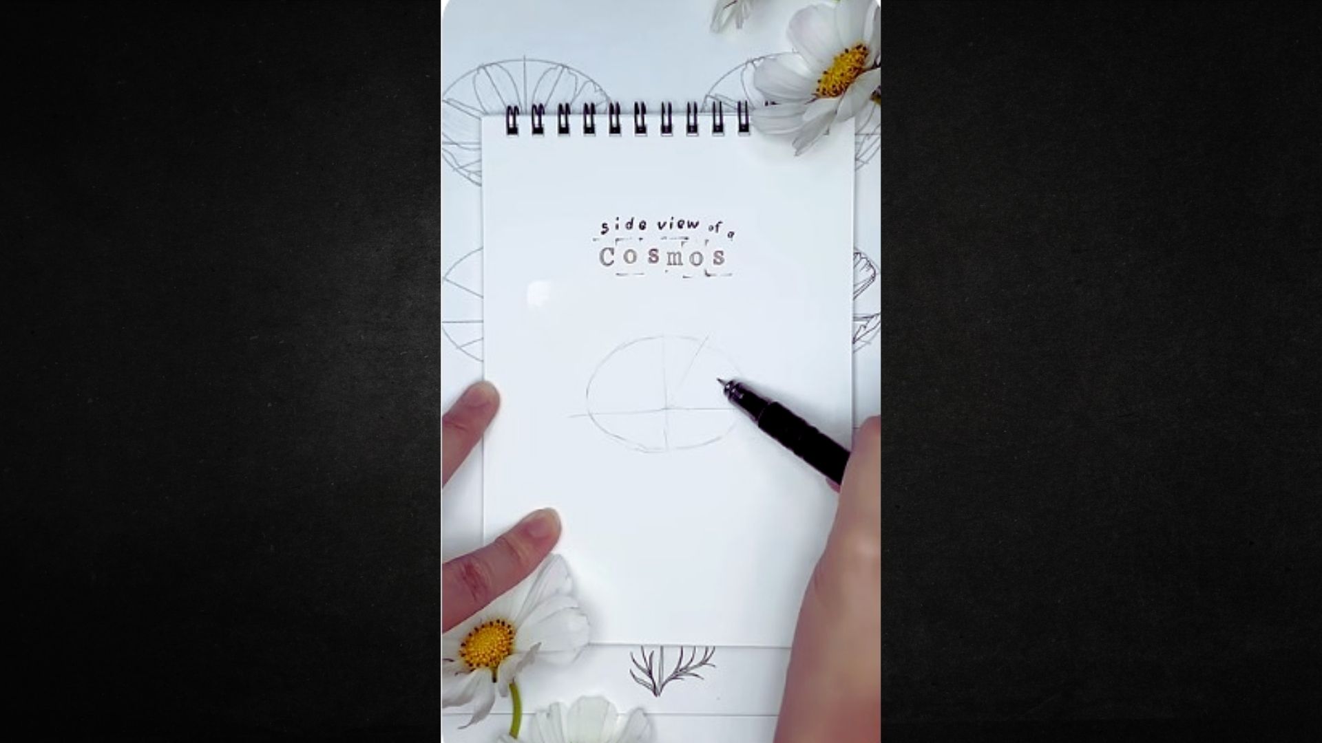 A person sketches on a notepad adorned with flowers, focusing intently on their drawing.