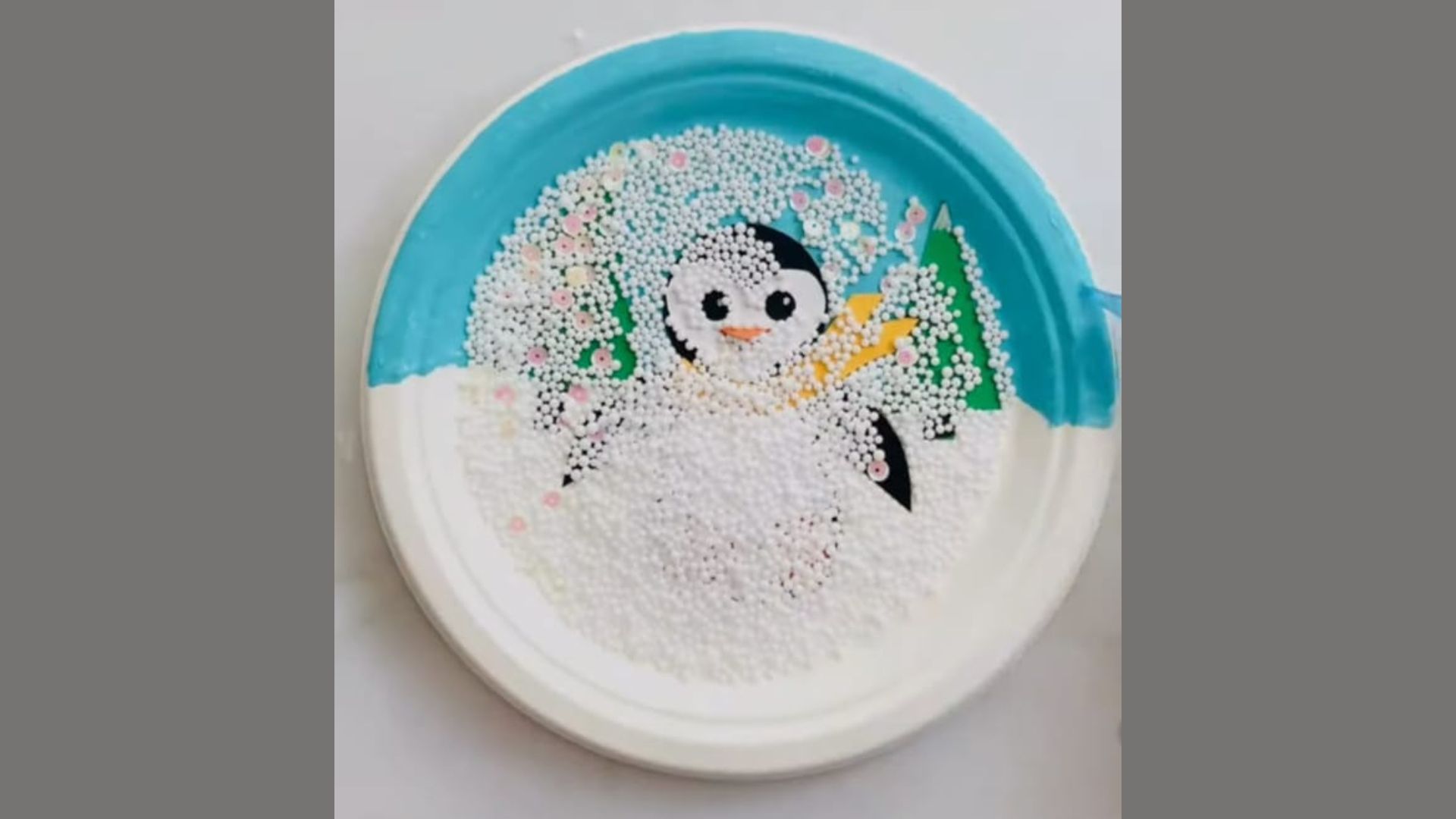 A paper plate featuring a hand-painted penguin design in black and white with a colorful background.