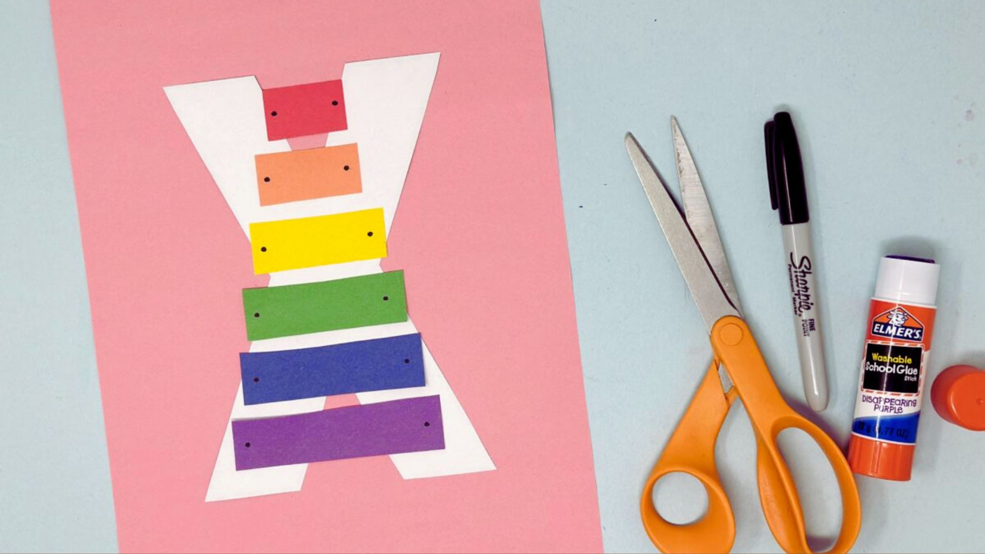 A vibrant rainbow-colored paper craft displayed alongside scissors and glue on a flat surface.