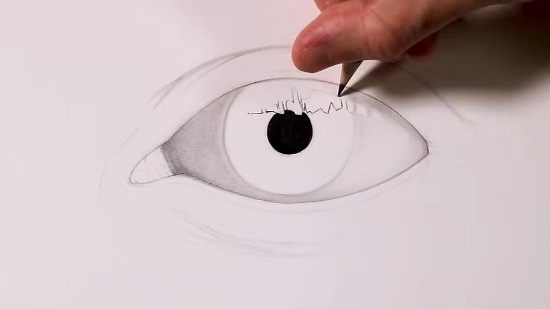 A person sketches an eye with a pencil, focusing intently on the details of the drawing.