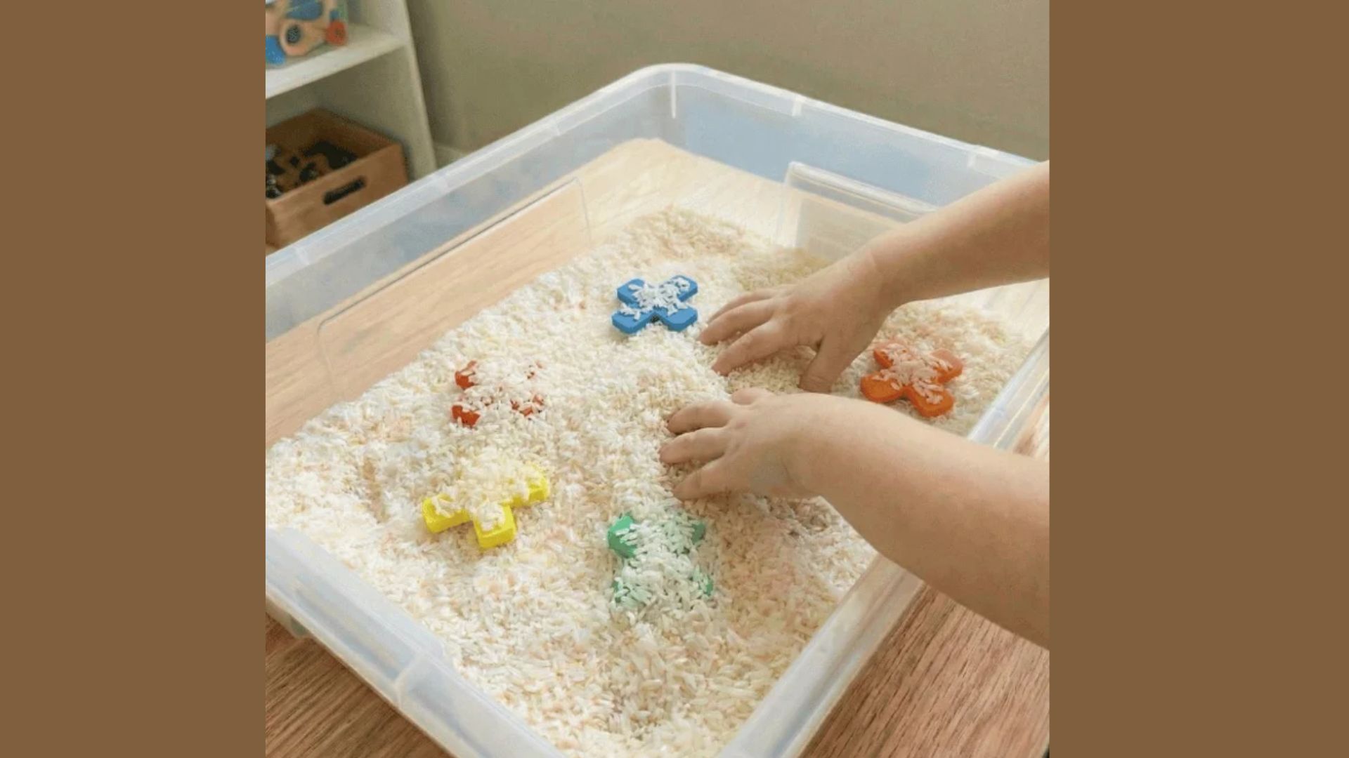 A child's hands play in a plastic container filled with uncooked rice, creating a sensory experience.