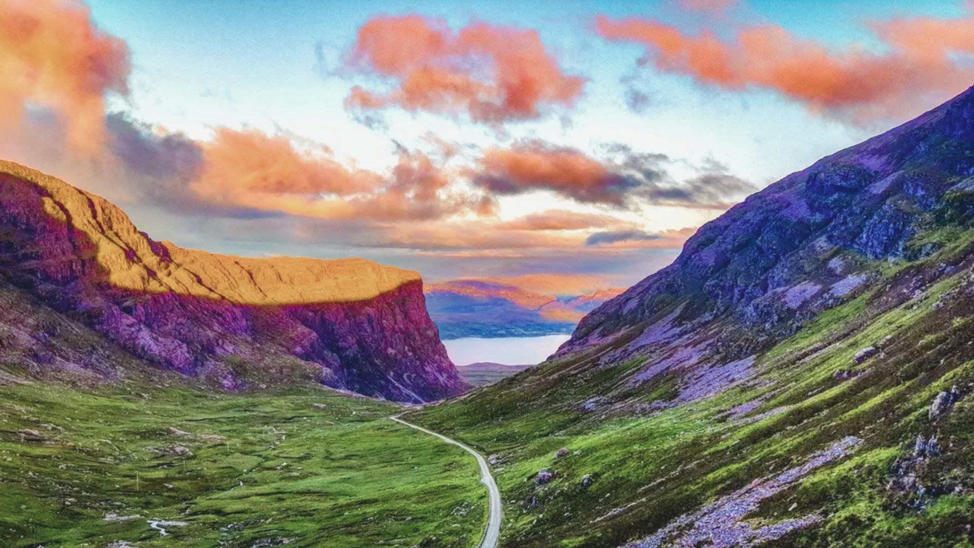 Scenic road winding through the lush greenery of the Scottish Highlands, leading to majestic mountain peaks.