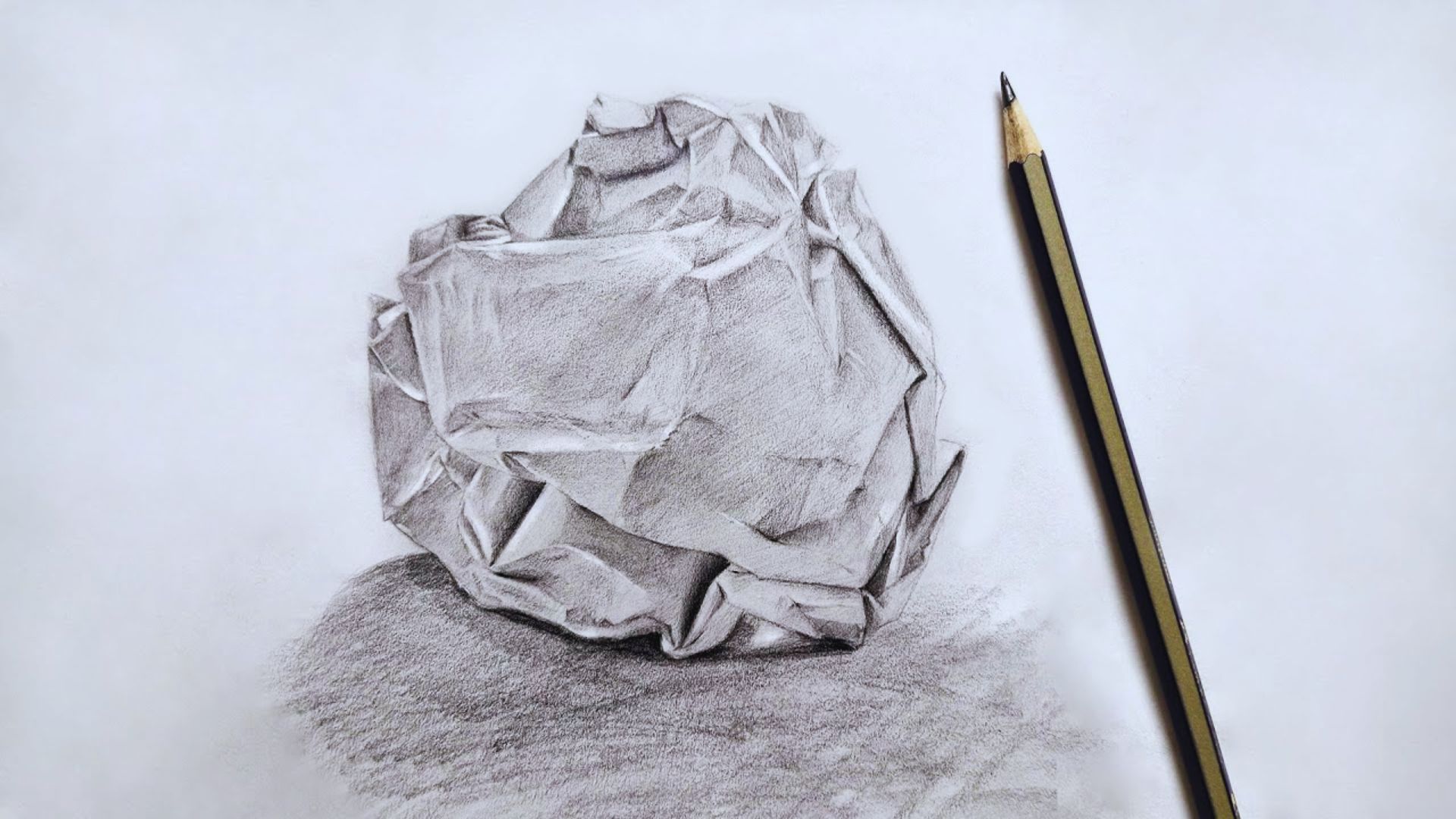 A pencil rests beside a crumpled piece of paper on a wooden table, suggesting a moment of creative frustration.