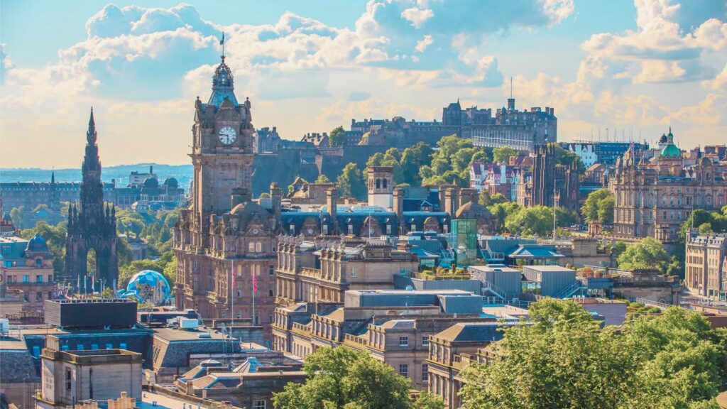 Edinburgh cityscape featuring the iconic castle prominently in the background against a clear blue sky.