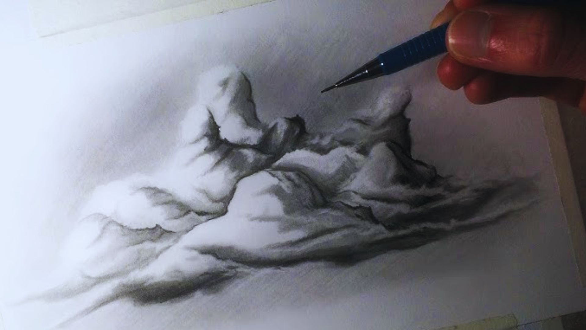 A person sketching a mountain landscape with a pencil on a blank sheet of paper.