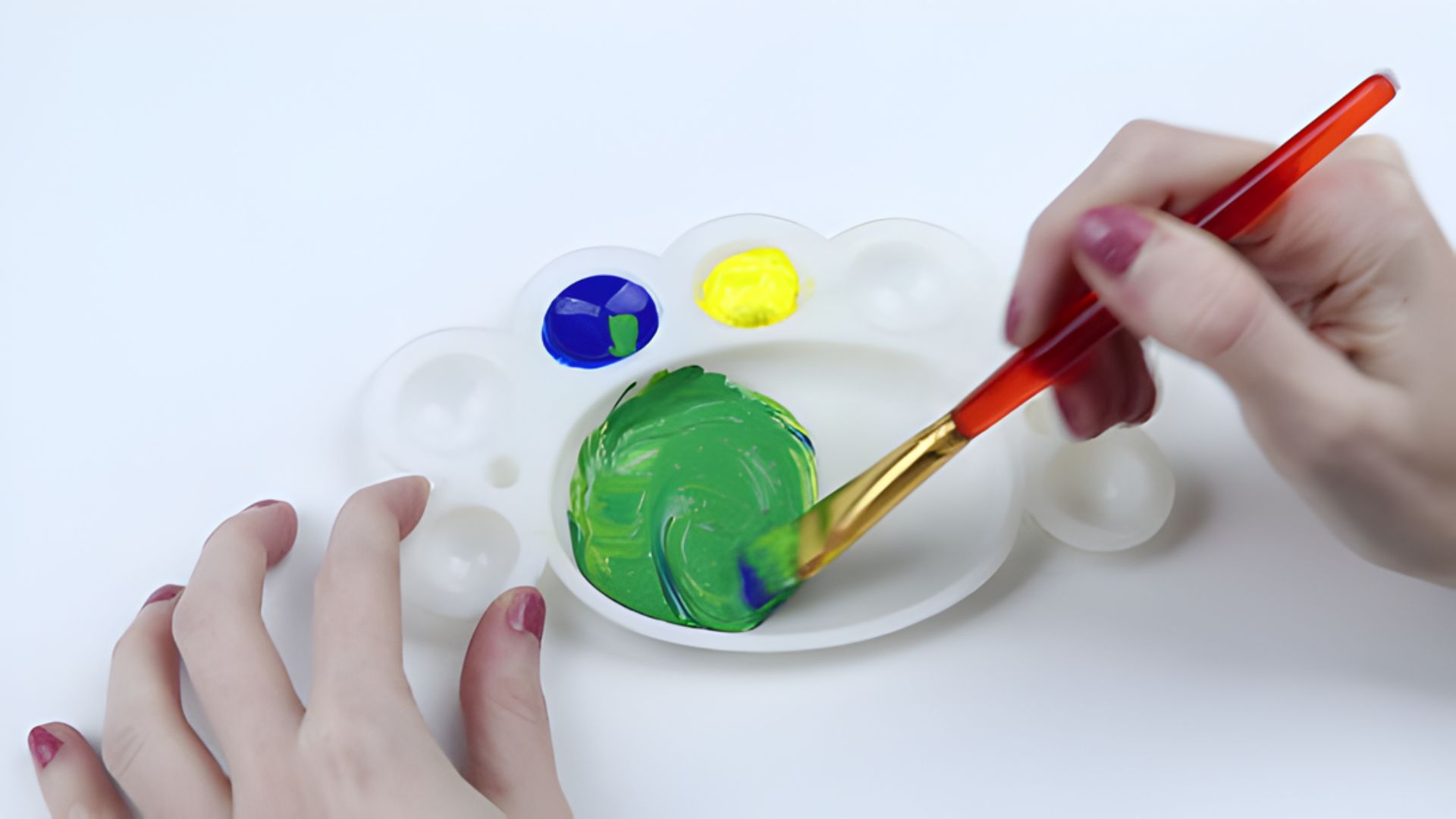 A person paints a green and yellow face with a brush, focusing intently on their artwork.