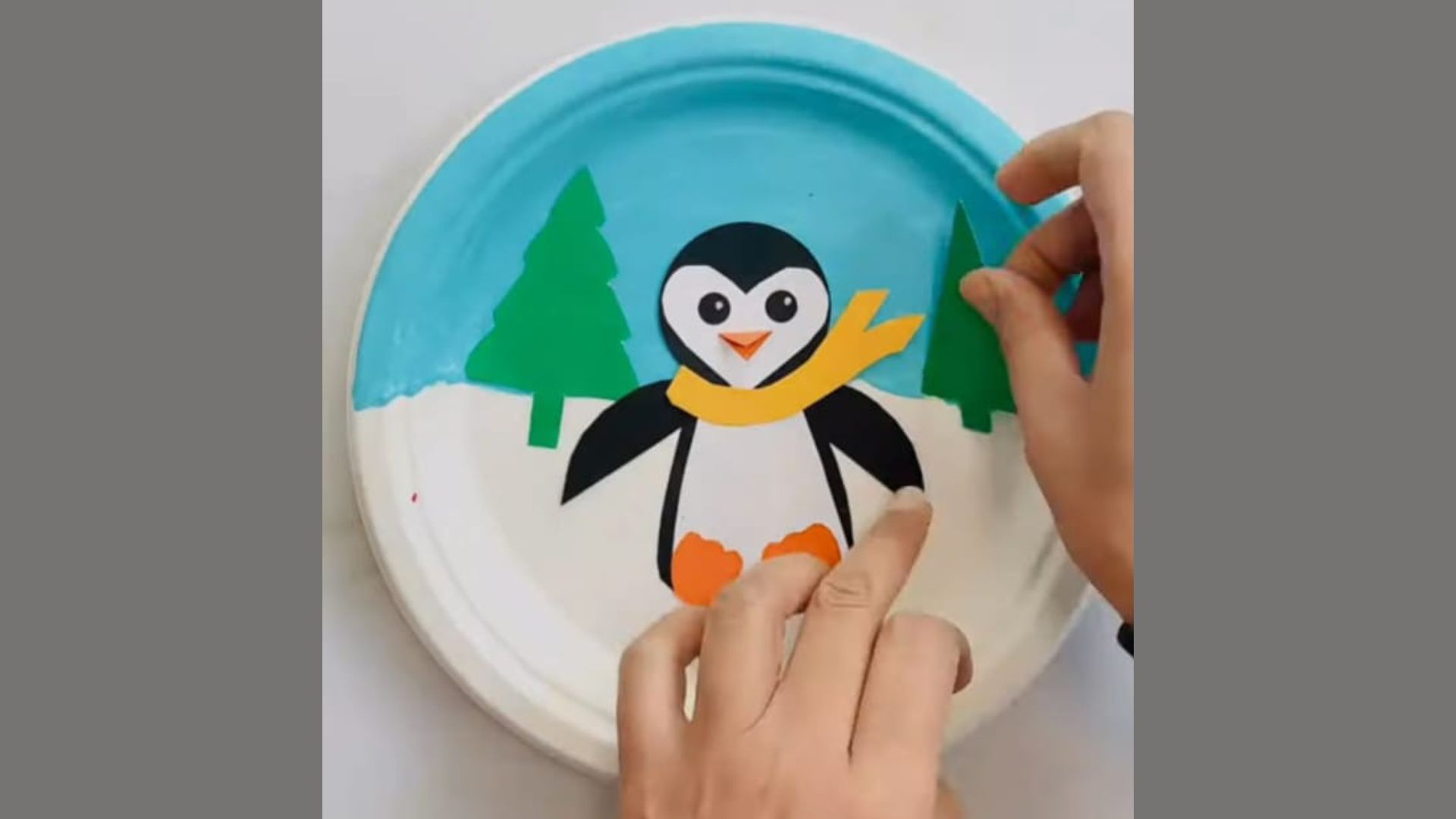A person paints a paper plate featuring a colorful penguin design, showcasing creativity and artistic expression.