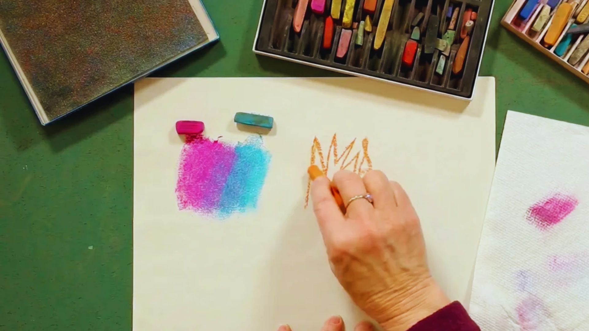 A person holds a paintbrush, creating artwork on a sheet of paper.