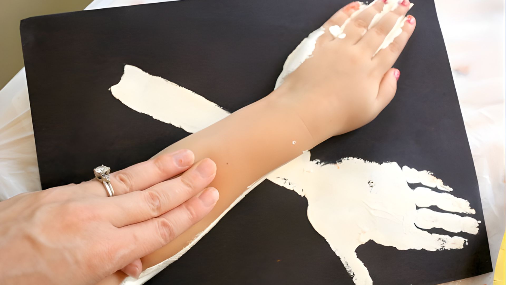 A person applies white paint to their hand, focusing on the details of the artwork.
