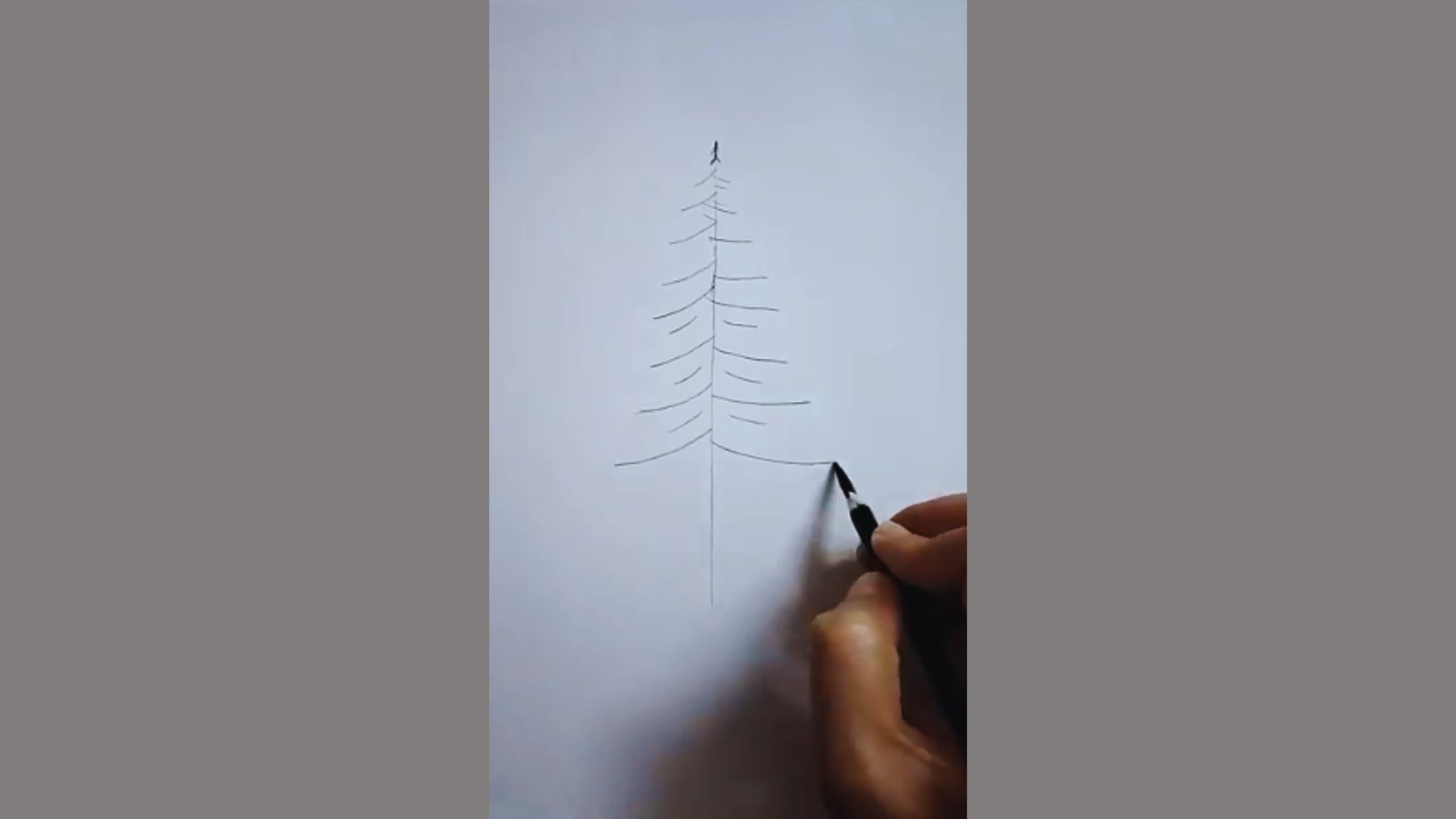 A hand drawing a Christmas tree with a pencil on a blank sheet of paper, showcasing the tree's outline and details.