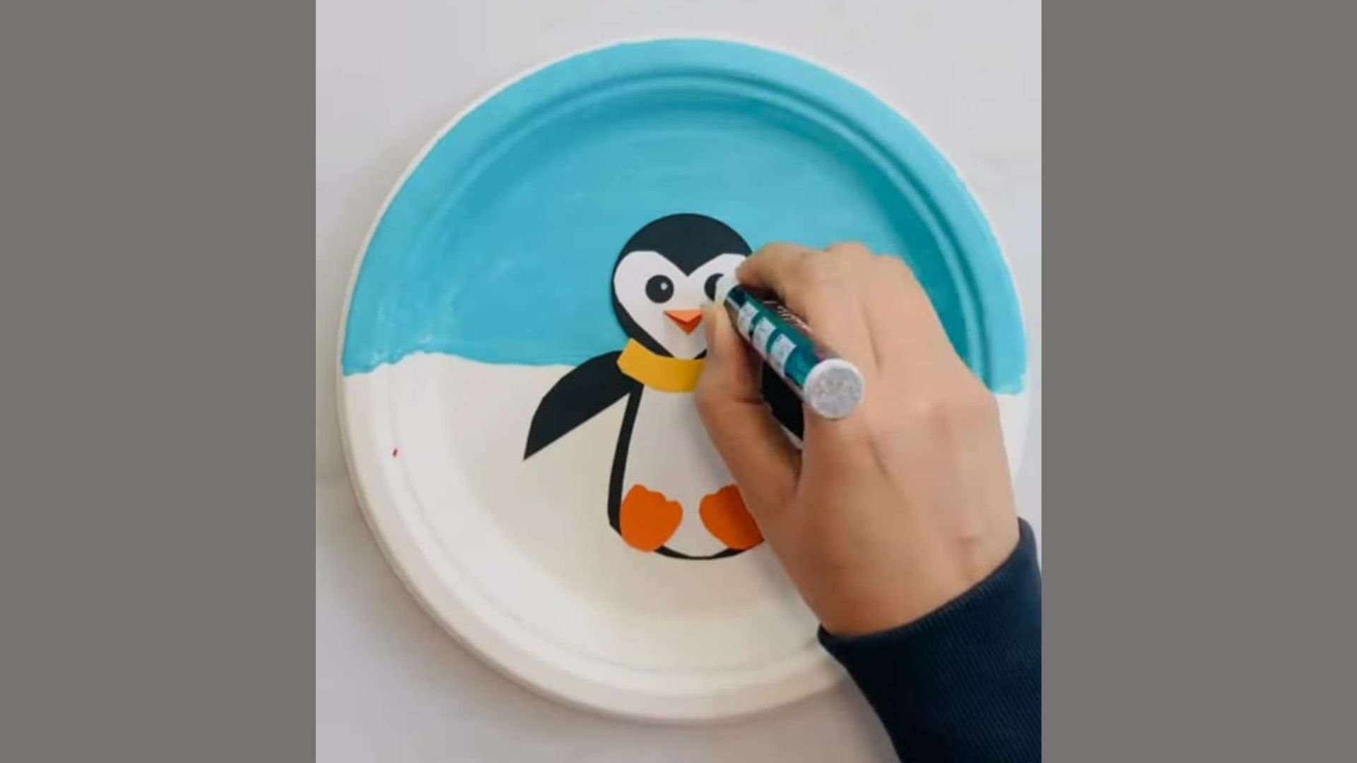 A person painting a colorful penguin design on a paper plate, showcasing creativity and artistic expression.