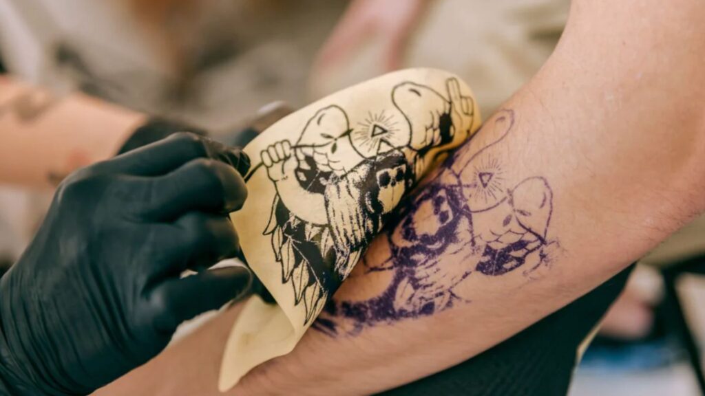 How to Transfer a Drawing Onto Skin Without Transfer Paper A person receiving a tattoo on their arm, with a tattoo artist focused on the design.