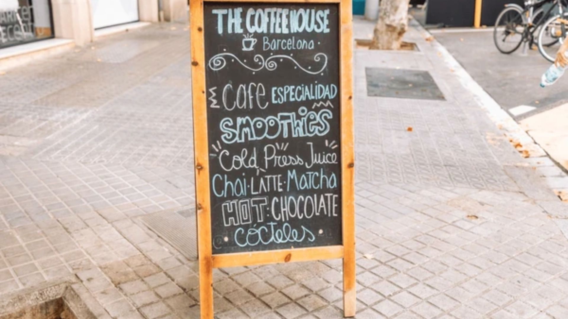 A sidewalk chalkboard sign displaying "The House of Coffee" in artistic lettering, inviting passersby to visit the coffee bar.