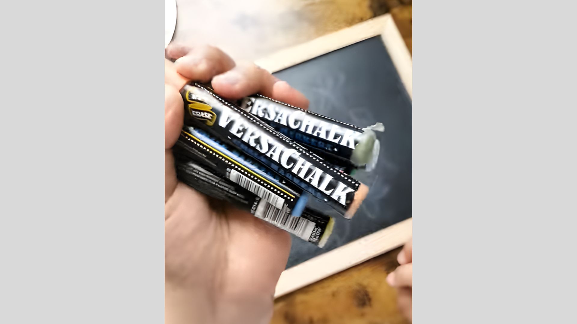 Hand holding colored chalk pieces near a small framed chalkboard, selecting colors.