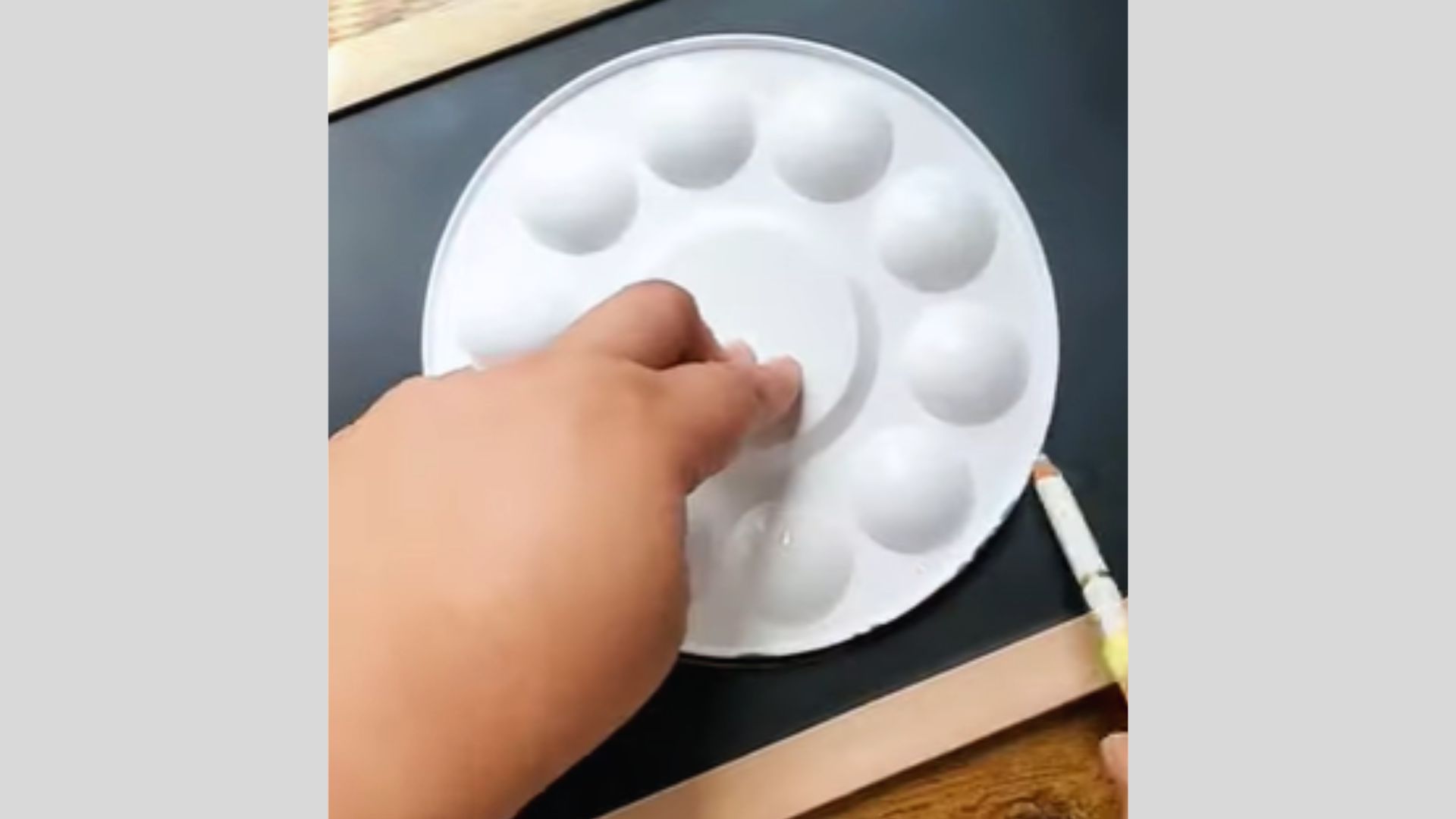 Hand uses a round paint palette to trace a perfect circle on the chalkboard surface.