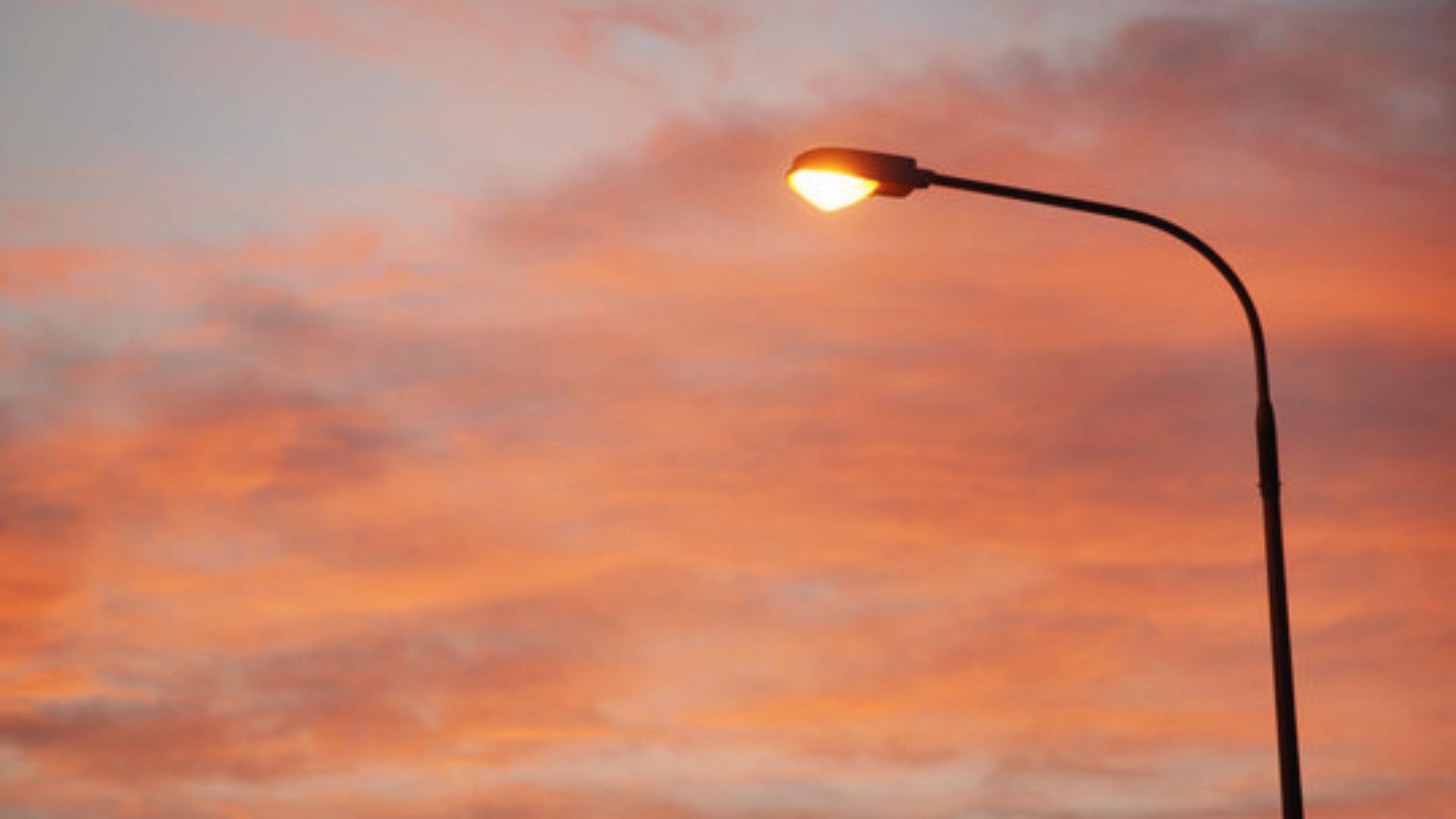 A glowing streetlamp against wispy orange and pink sunset clouds, a simple real-life cloud reference for easy evening sky drawings.
