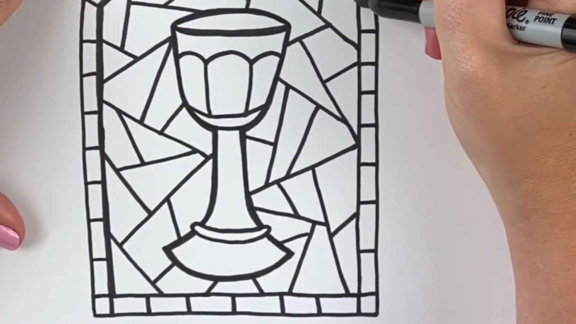"A person sketches a stained glass design on paper, focusing intently on the intricate details of the artwork."