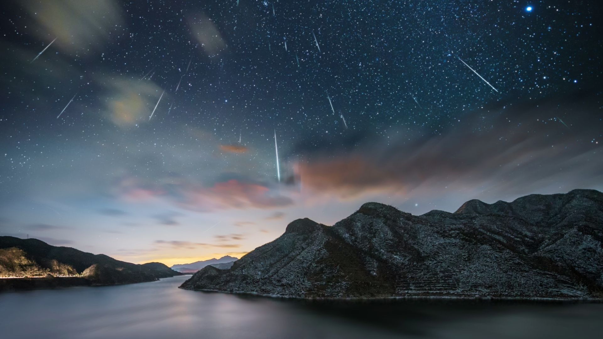 A meteor shower streaking over dark mountains and wispy clouds at twilight, real life reference for drawing night sky clouds.