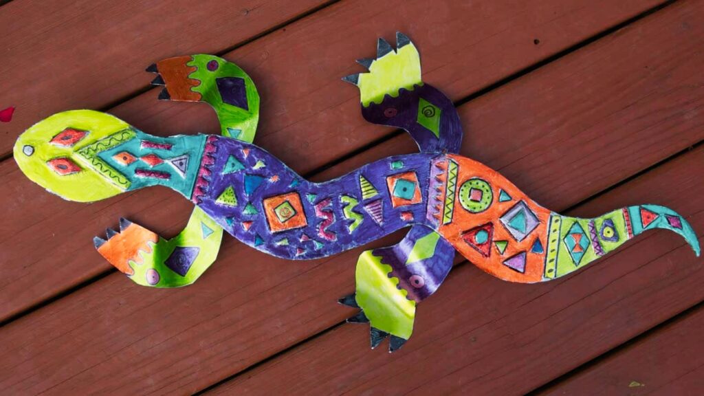Colorful paper cutout lizard decorated with geometric patterns in purple, orange, green, and blue.