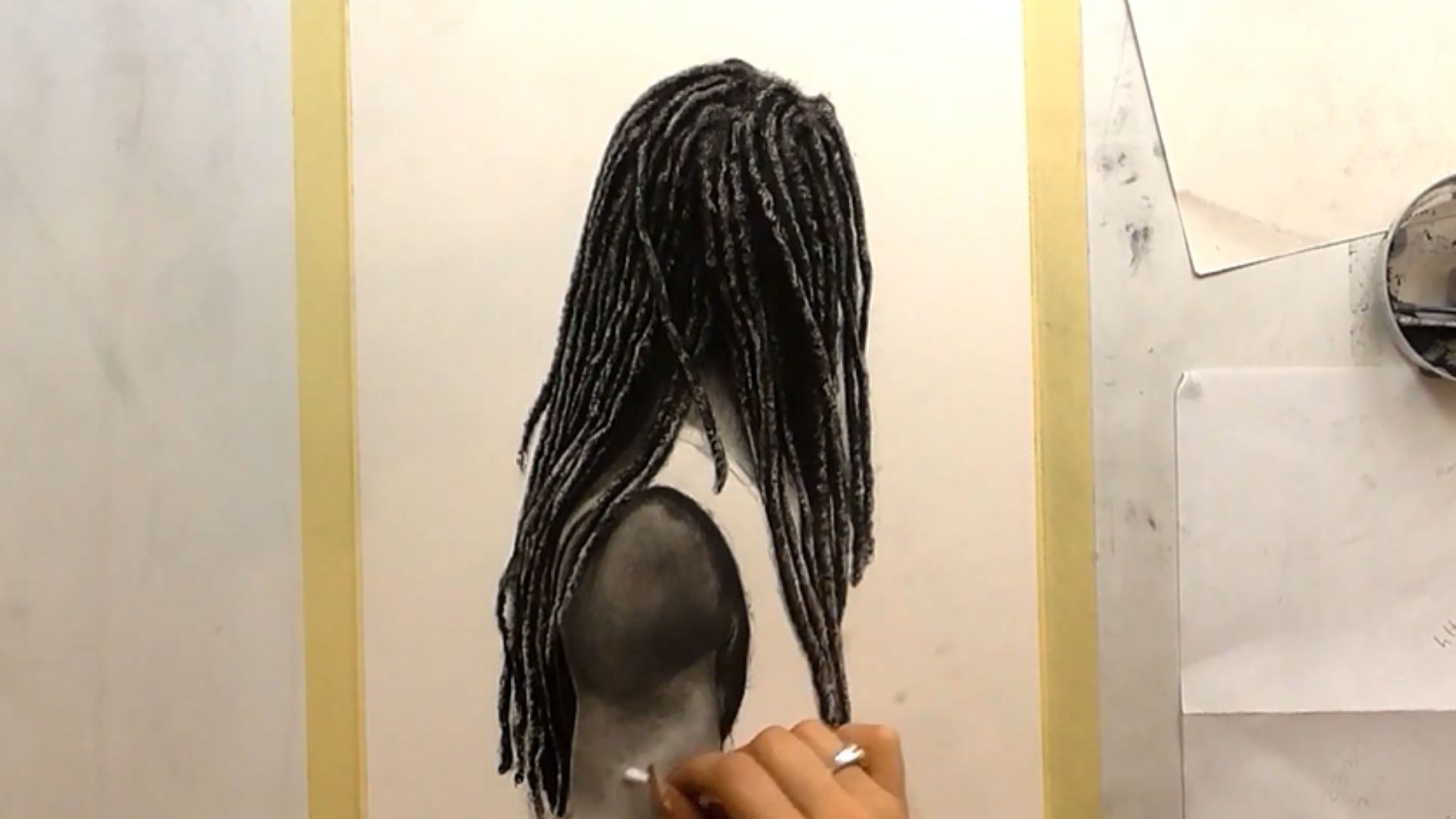 "A person sketches a woman with dreadlocks, focusing on her hairstyle and facial features."