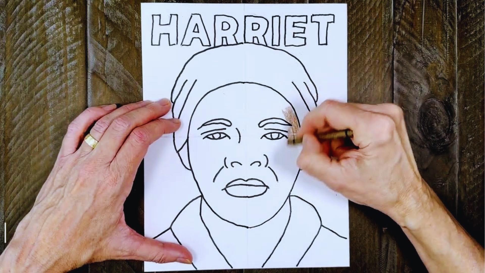 Hand coloring Harriet Tubman portrait outline with brown crayon on white paper on wood table.