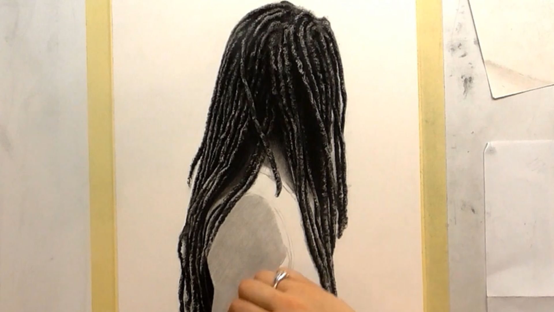 "A person sketches a black and white portrait of a woman with dreadlocks on a blank canvas."