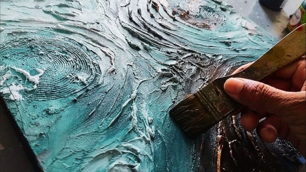 A person painting with a brush on a canvas covered in blue paint.
