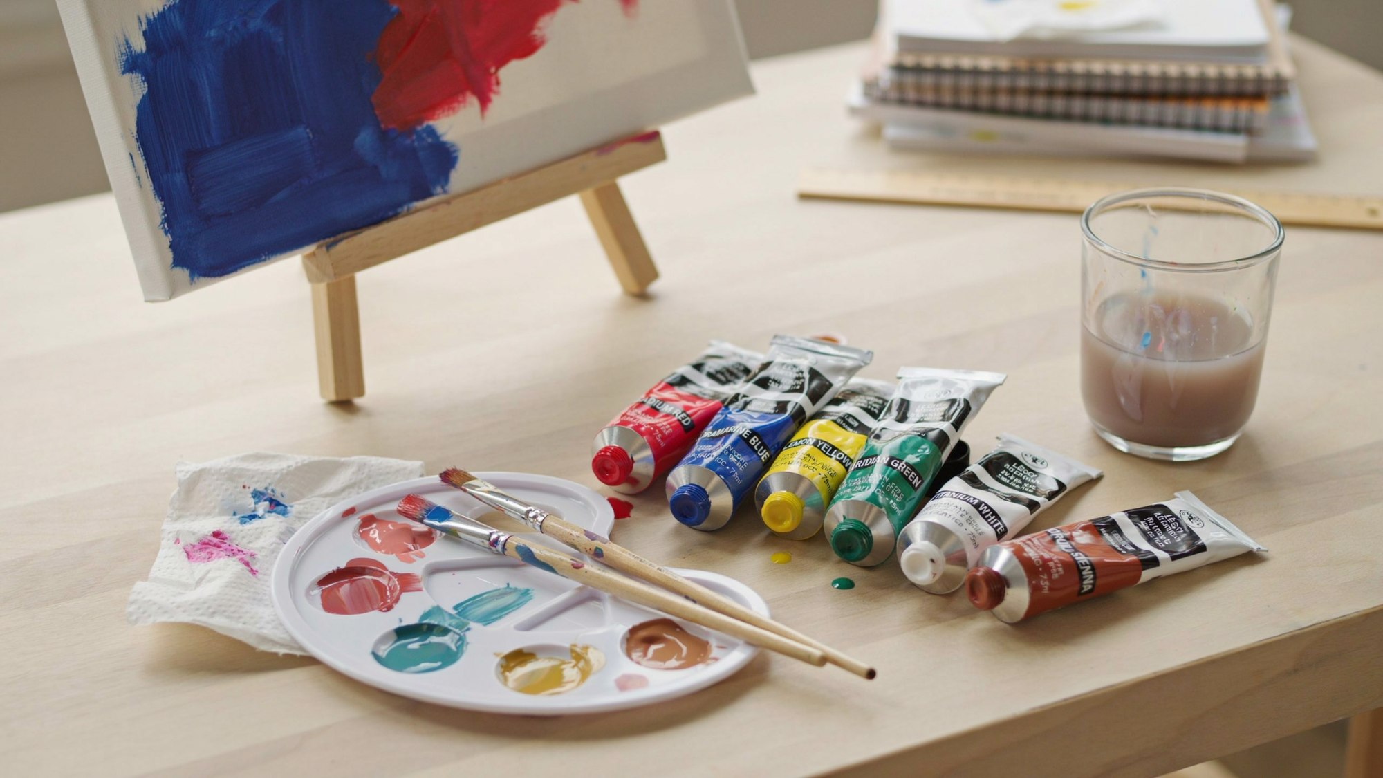 Acrylic paint tubes, brushes, and a colorful canvas displayed in an artist’s studio workspace.