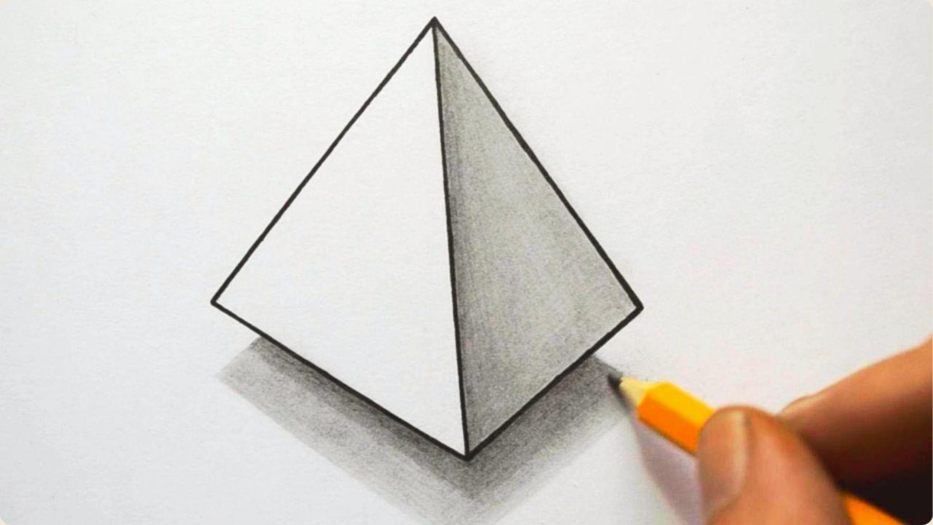 A hand uses a yellow pencil to shade the cast shadow of a 3D triangular pyramid on white paper.